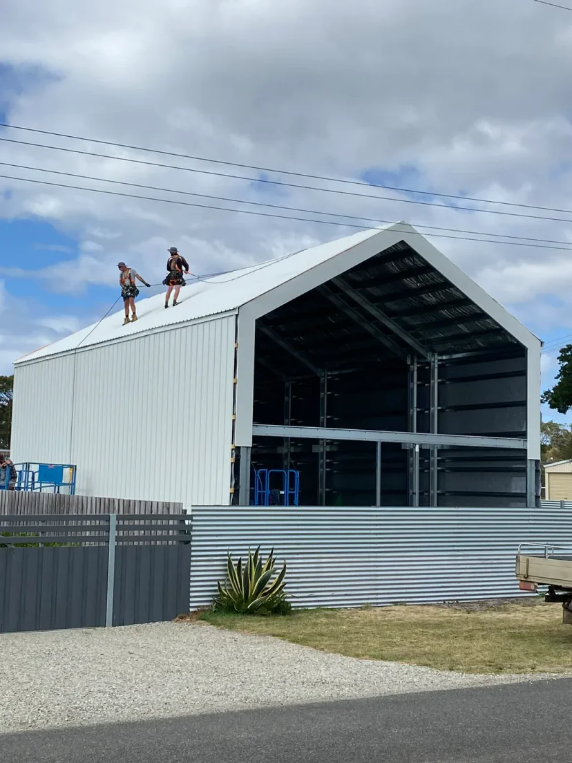 Two workers standing on the ridge of Shed Home #03 as the roof sheeting goes on