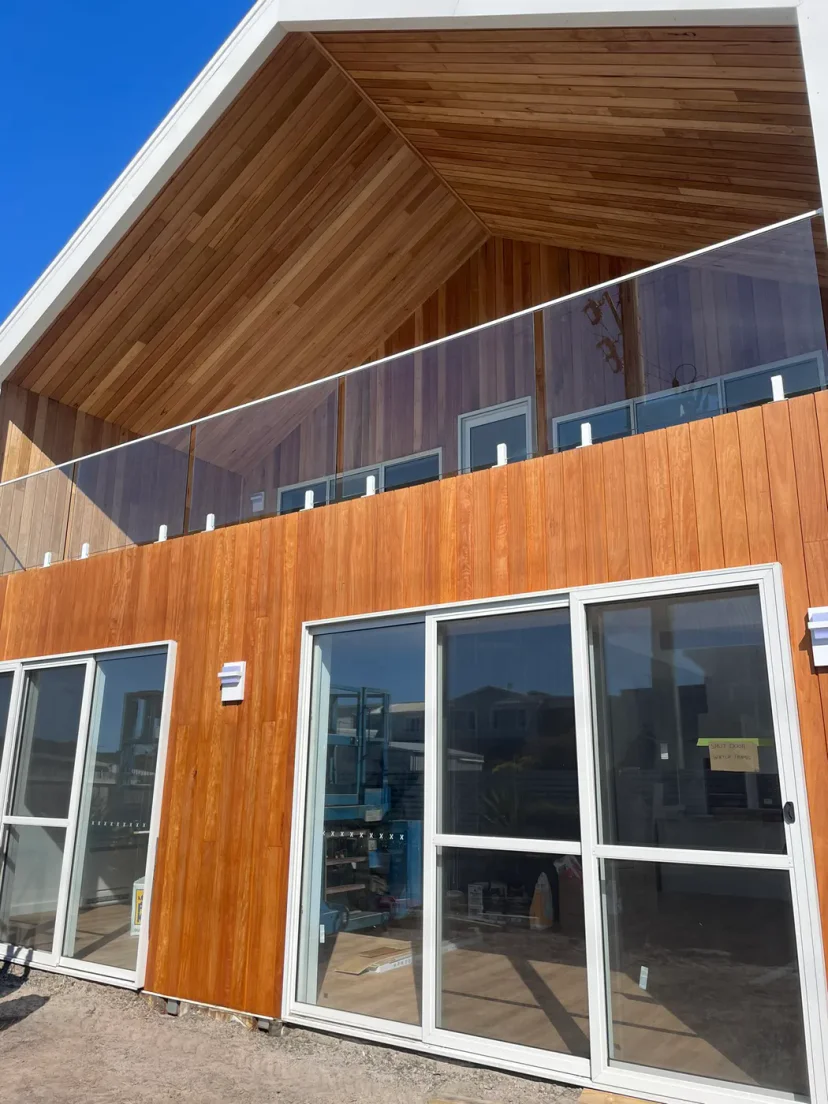 The finished Shed Home #03 exterior — timber-clad gable, glass balustrade and upper deck
